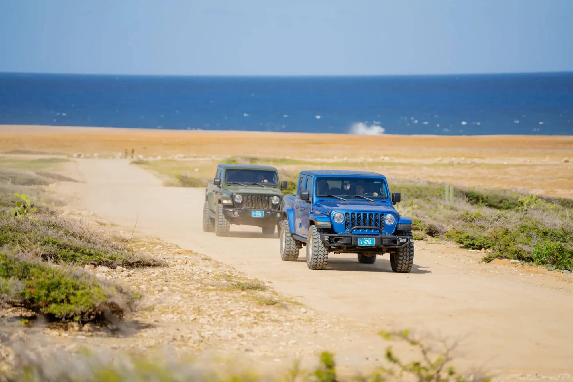 Two Jeeps coming up a sandy coastal track toward the camera with the sea behind them in Aruba
