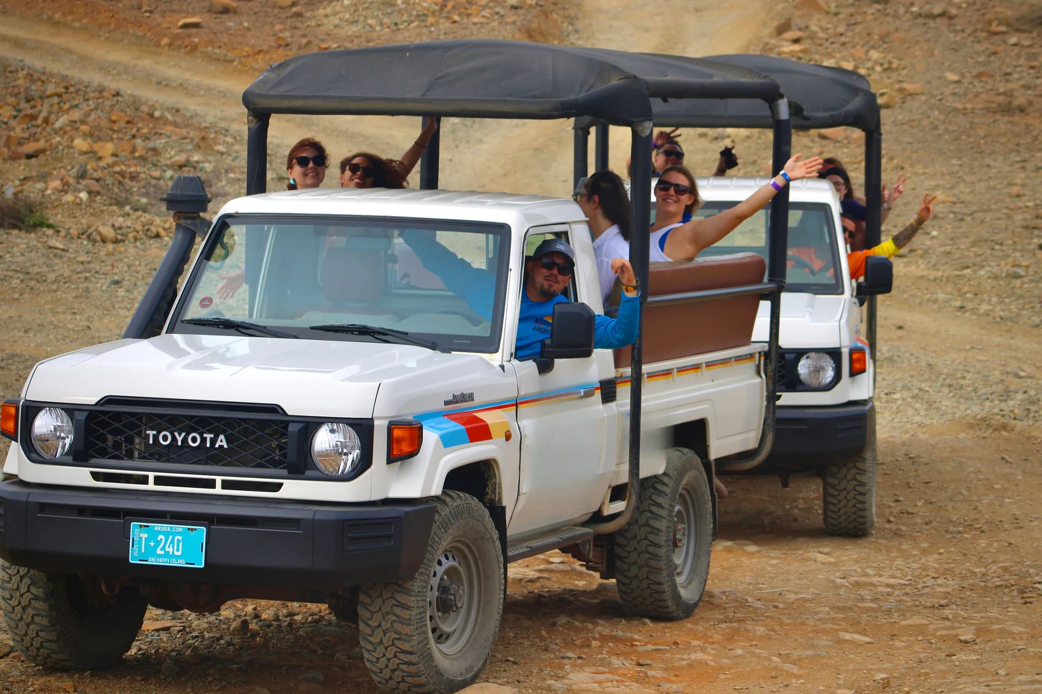 Two open-air safari 4x4s full of waving guests on the dirt trail into Arikok National Park
