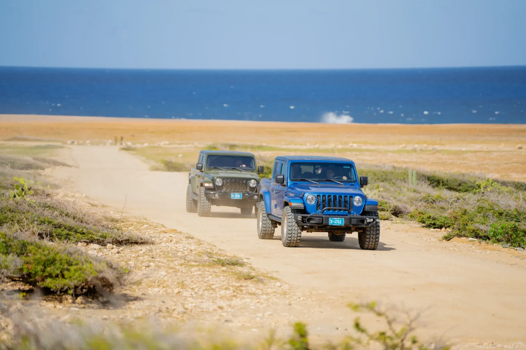 Two Jeeps coming up a sandy coastal track toward the camera with the sea behind them in Aruba