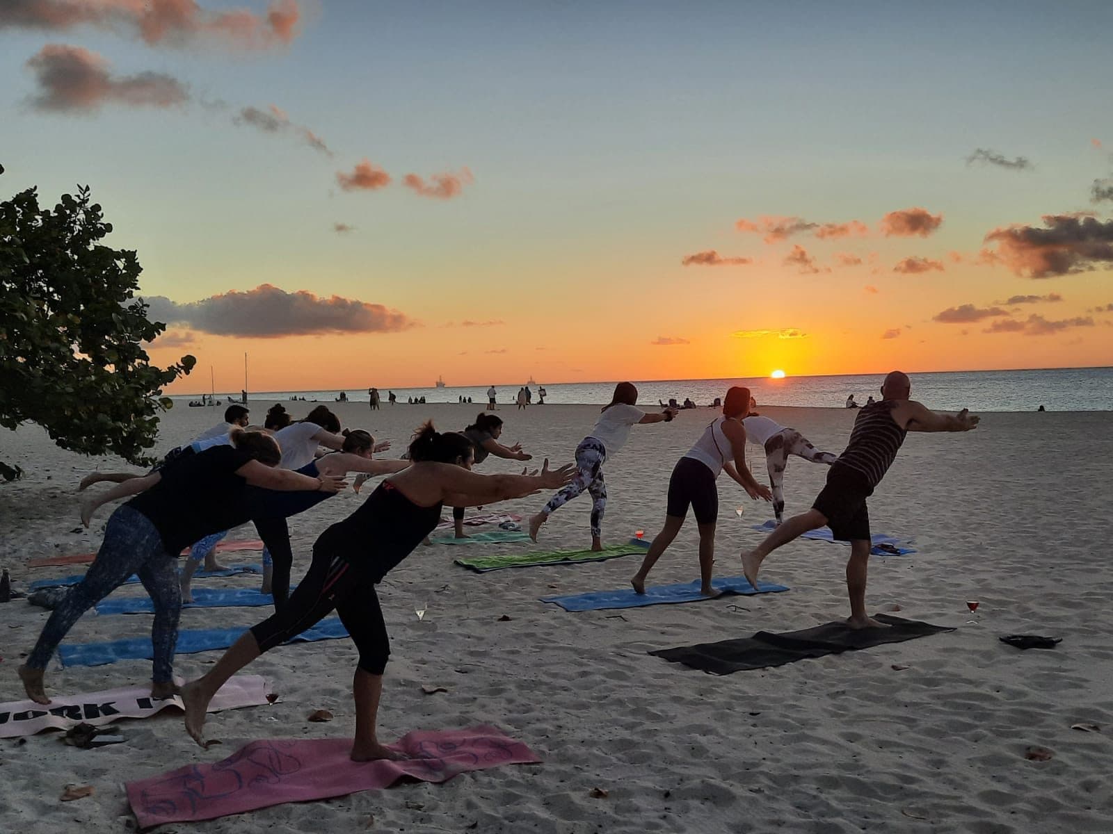 A beach yoga class mid-pose on Eagle Beach with the sun low over the sea