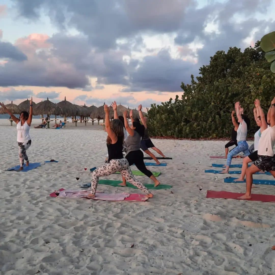 Guests in warrior pose with the palapas of Eagle Beach behind them