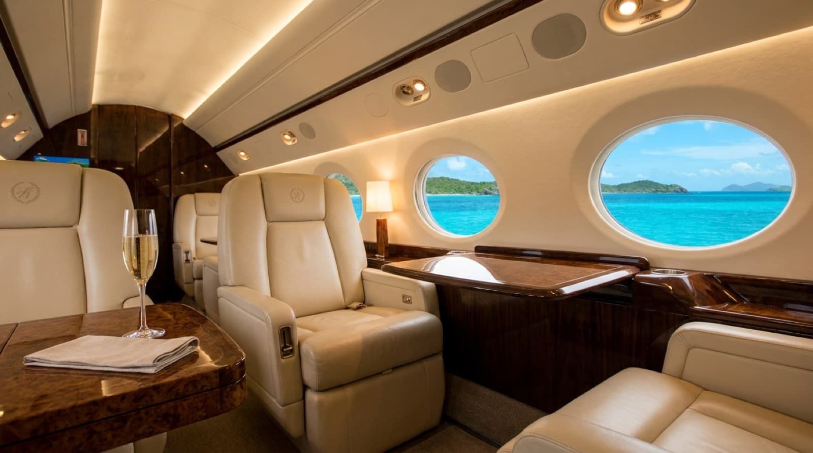 The cream-leather cabin of a private jet with the turquoise Caribbean through the windows