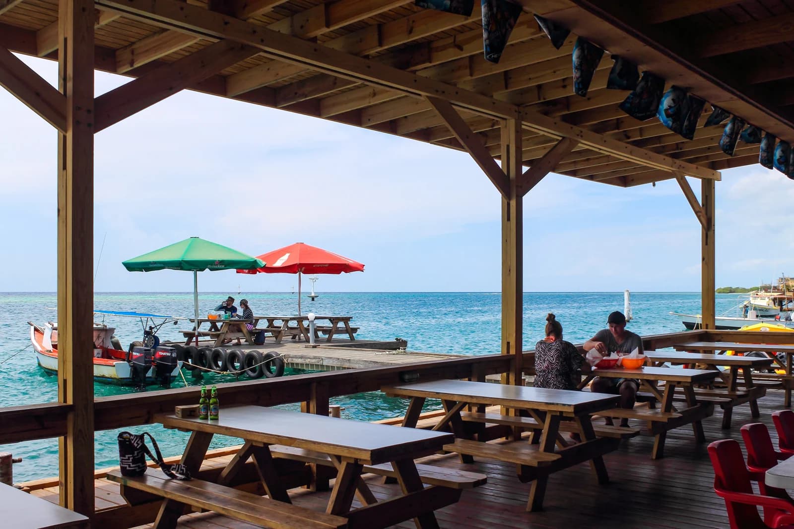 Wooden picnic tables, diners and fishing boats beside the waterfront at Zeerovers in Savaneta, Aruba