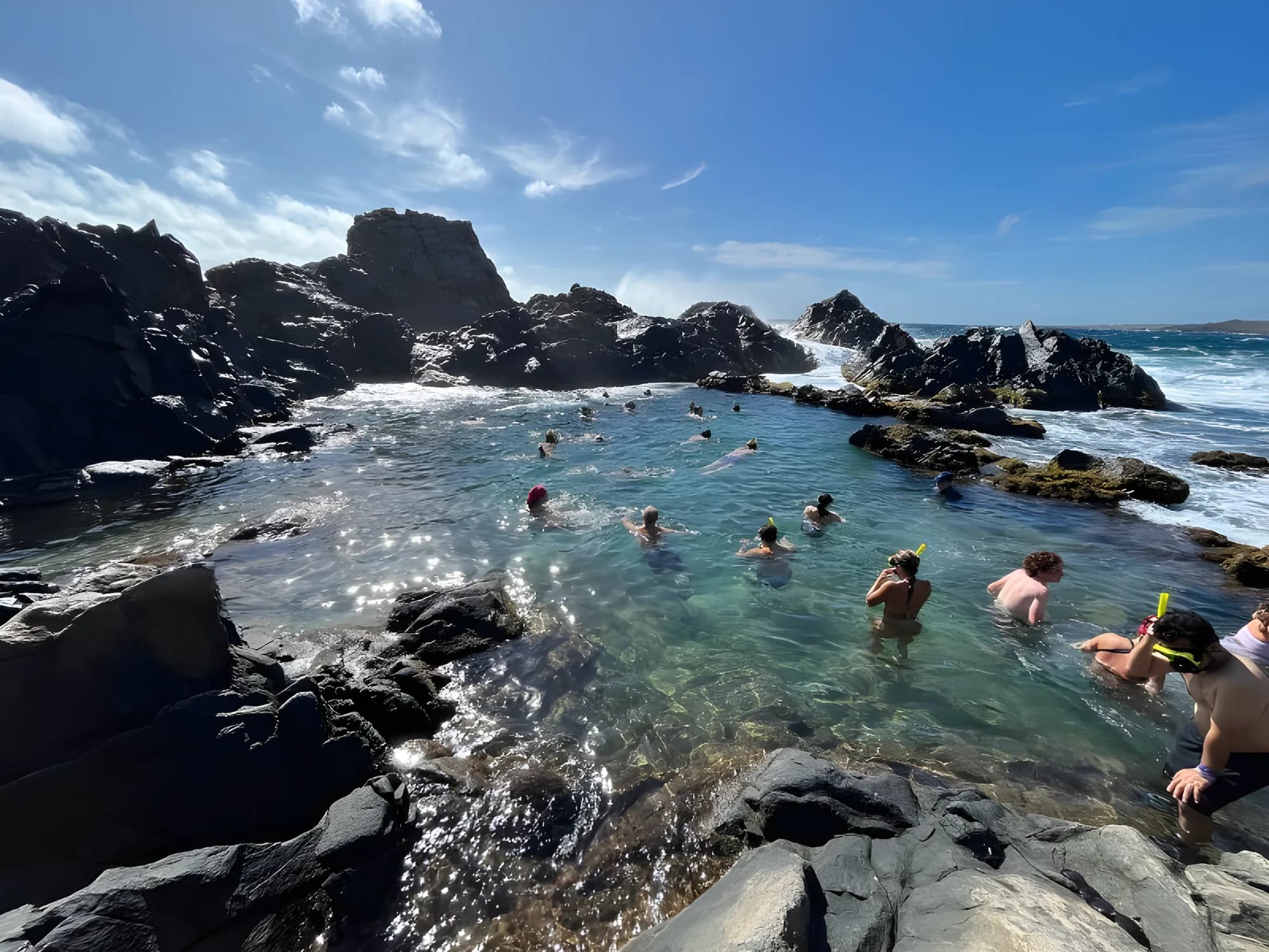 Swimmers floating in the Natural Pool inside its ring of black volcanic rock