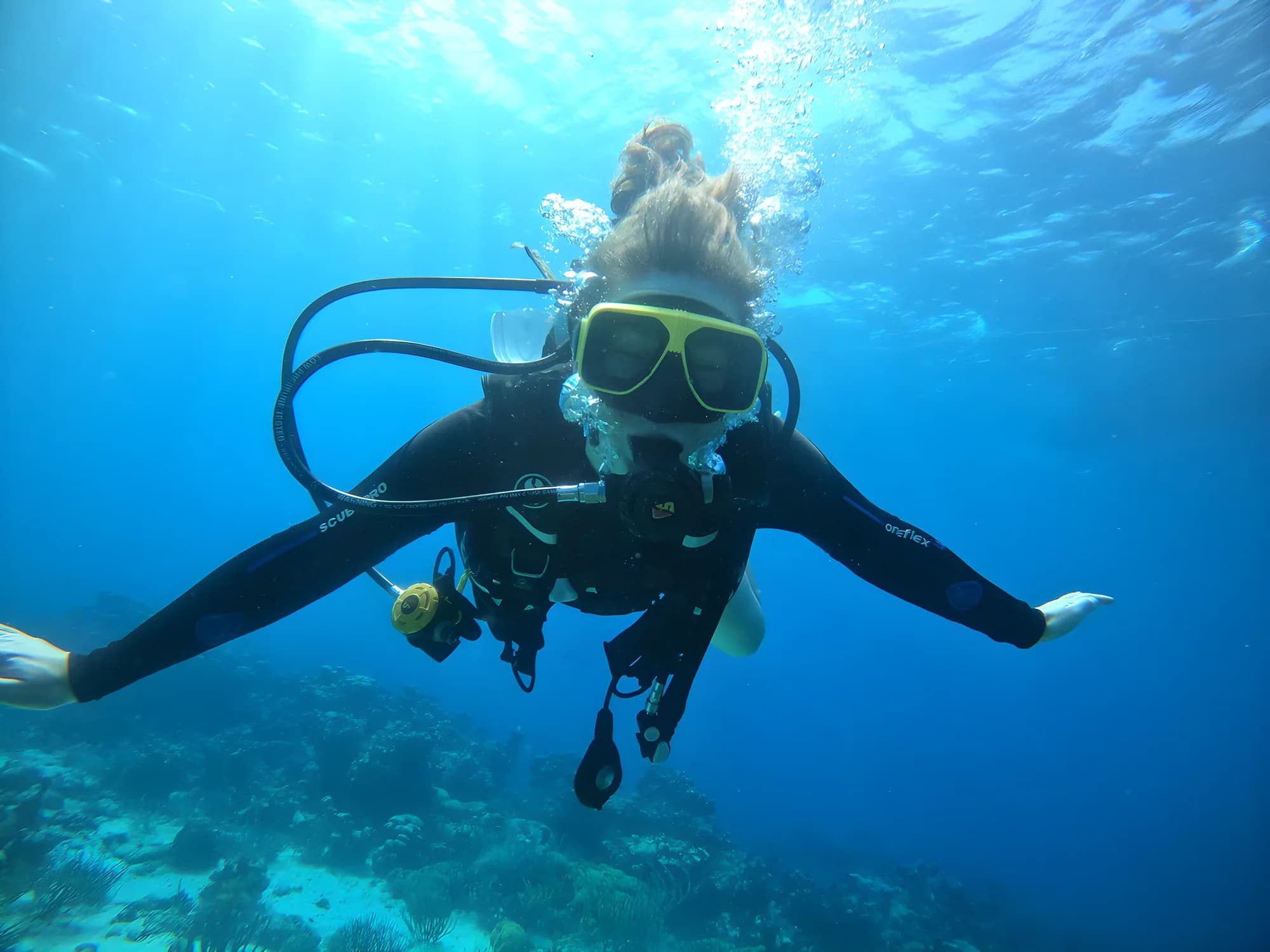 A diver in a yellow mask hovering in clear blue water above the reef