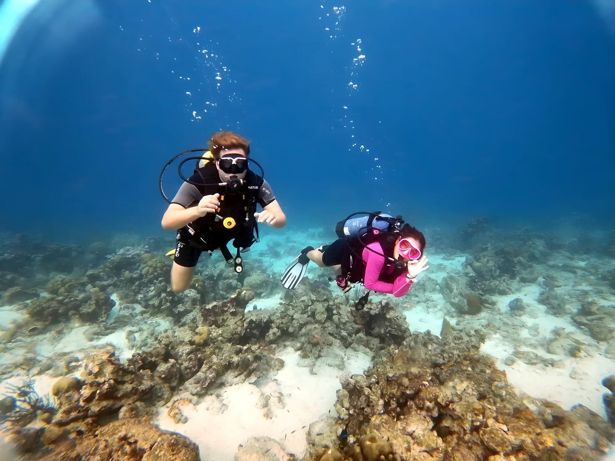 Two divers giving the OK sign over a coral reef in clear blue water