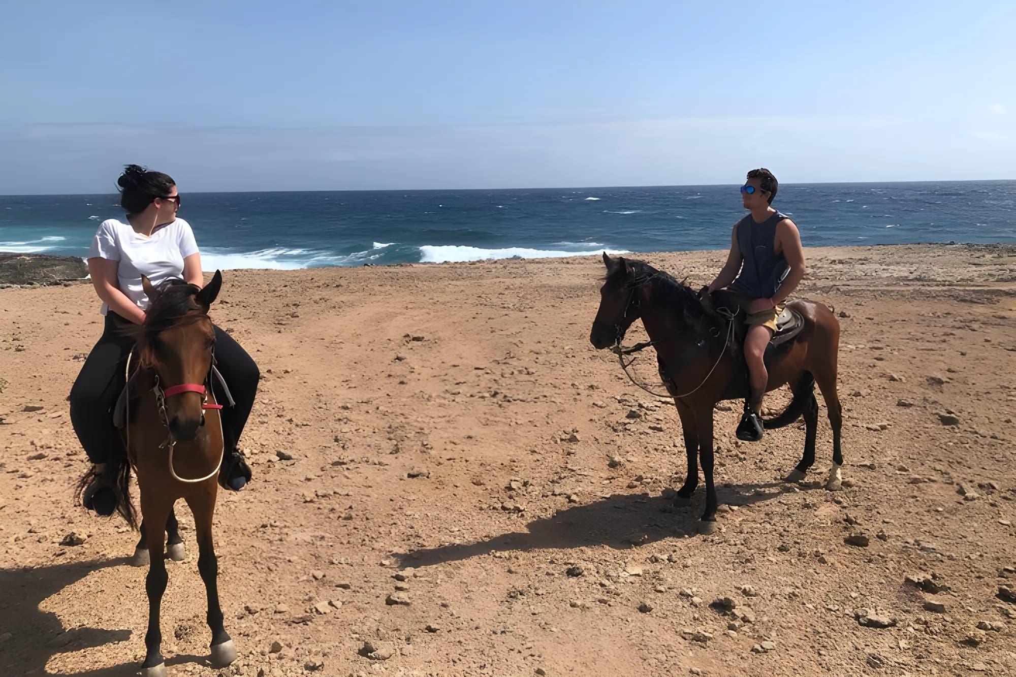 Two riders on horseback crossing the open coastal plain with the sea behind