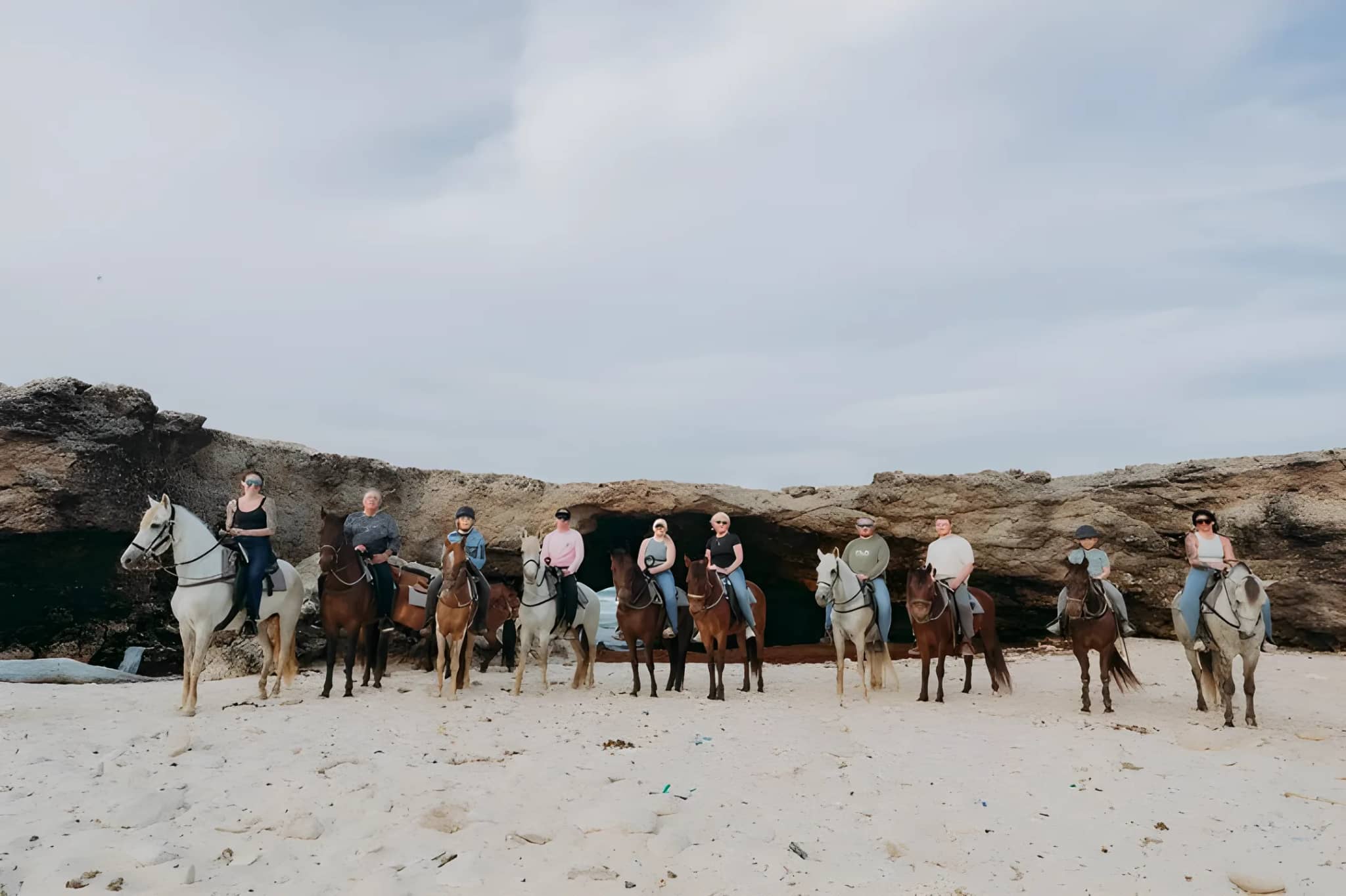A line of riders on horseback under a small natural rock bridge on a north coast beach in Aruba