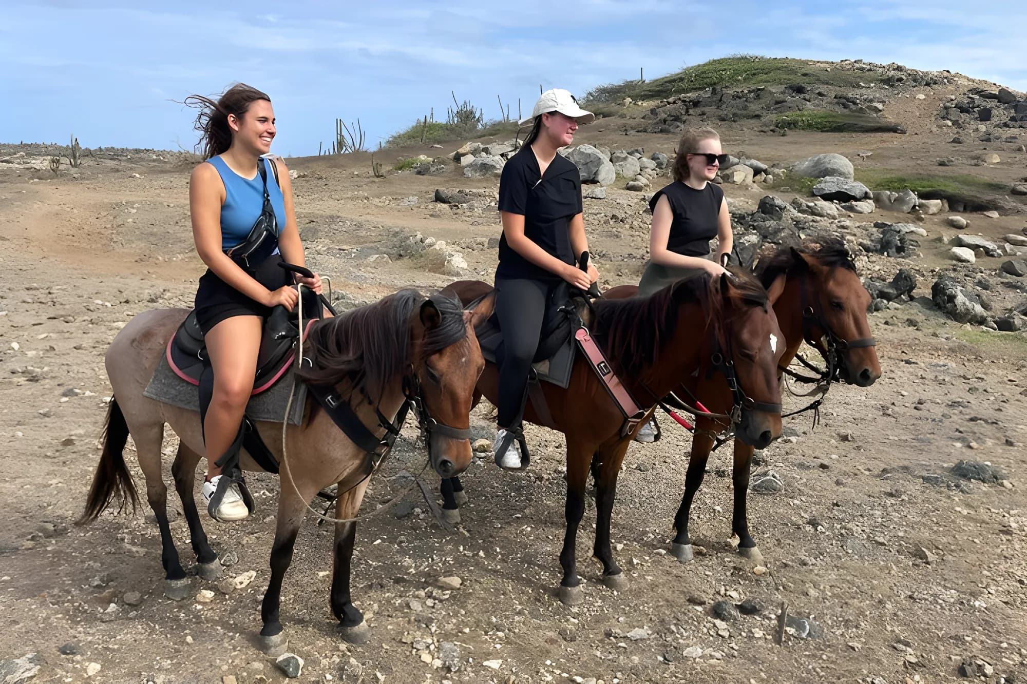 Three riders on horseback pausing on a rocky hillside in the Aruban countryside
