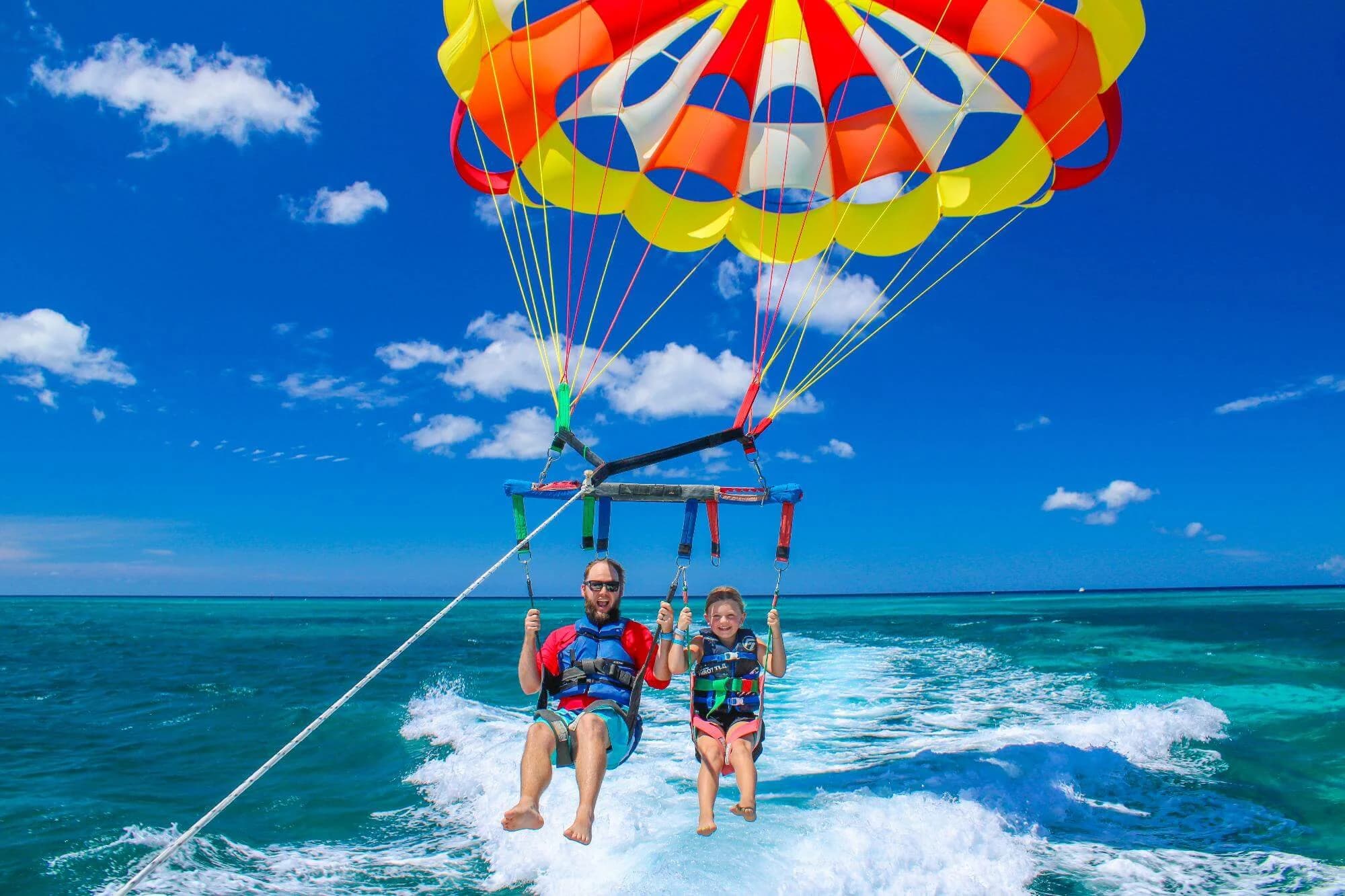 Two guests beneath the crew’s multicolored parasail off Palm Beach, Aruba