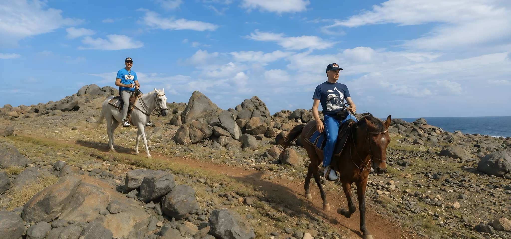 Two riders on horseback crossing the rocky north coast of Aruba