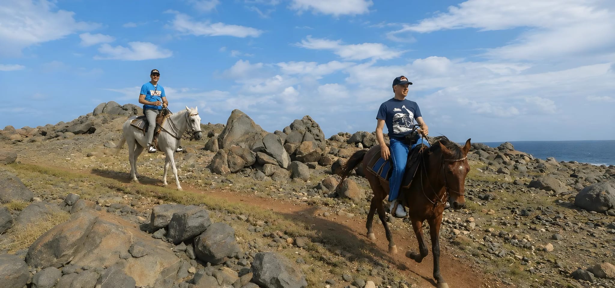 Two riders on horseback crossing the rocky north coast of Aruba