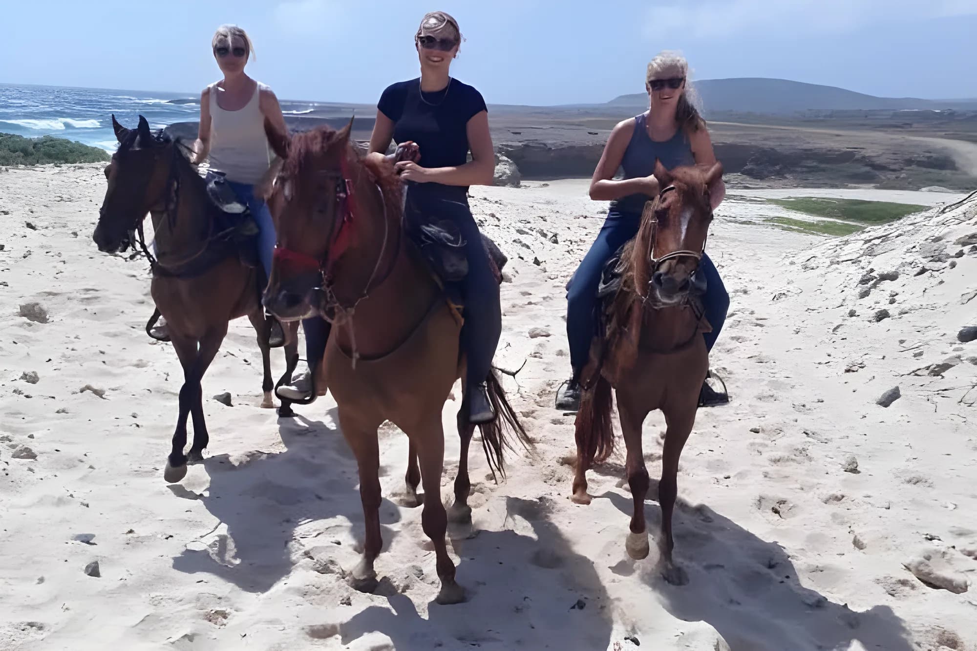 Three riders on horseback crossing white sand dunes