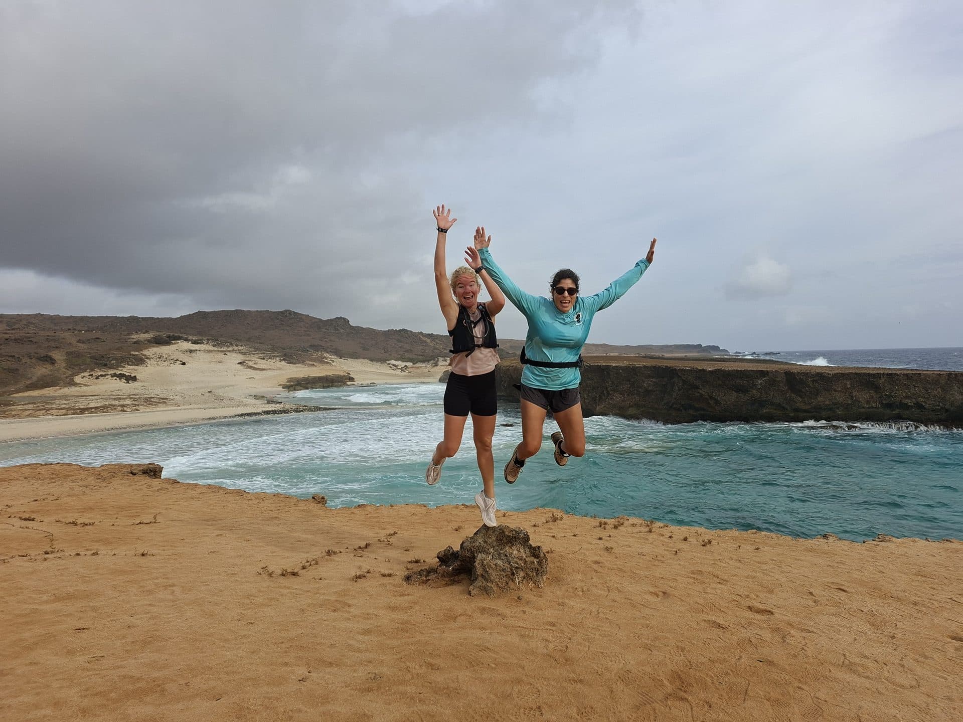 Two hikers jumping for joy above a turquoise cove on the north coast of Aruba