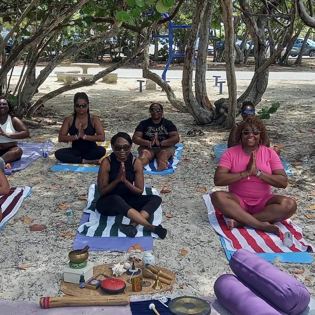 Guests seated in a circle with hands at heart center under the sea grape trees