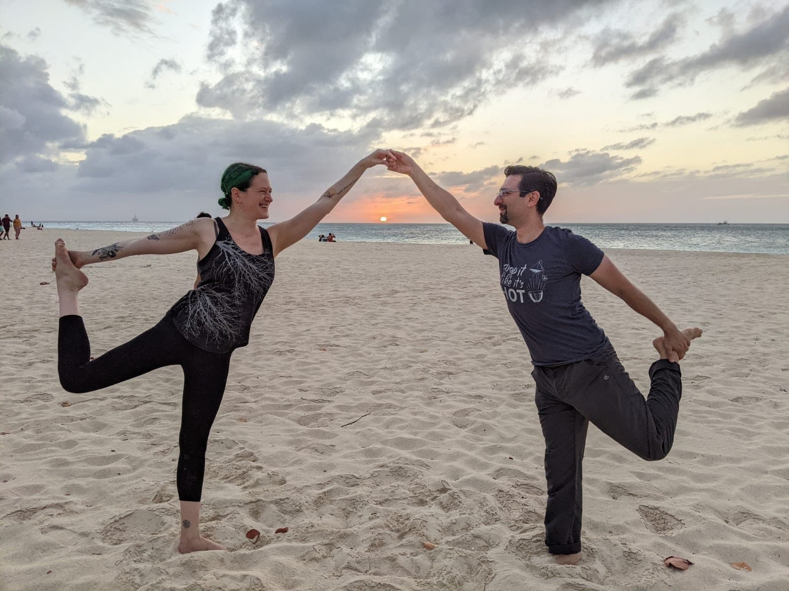 Two guests holding hands in dancer pose at sunset on Eagle Beach
