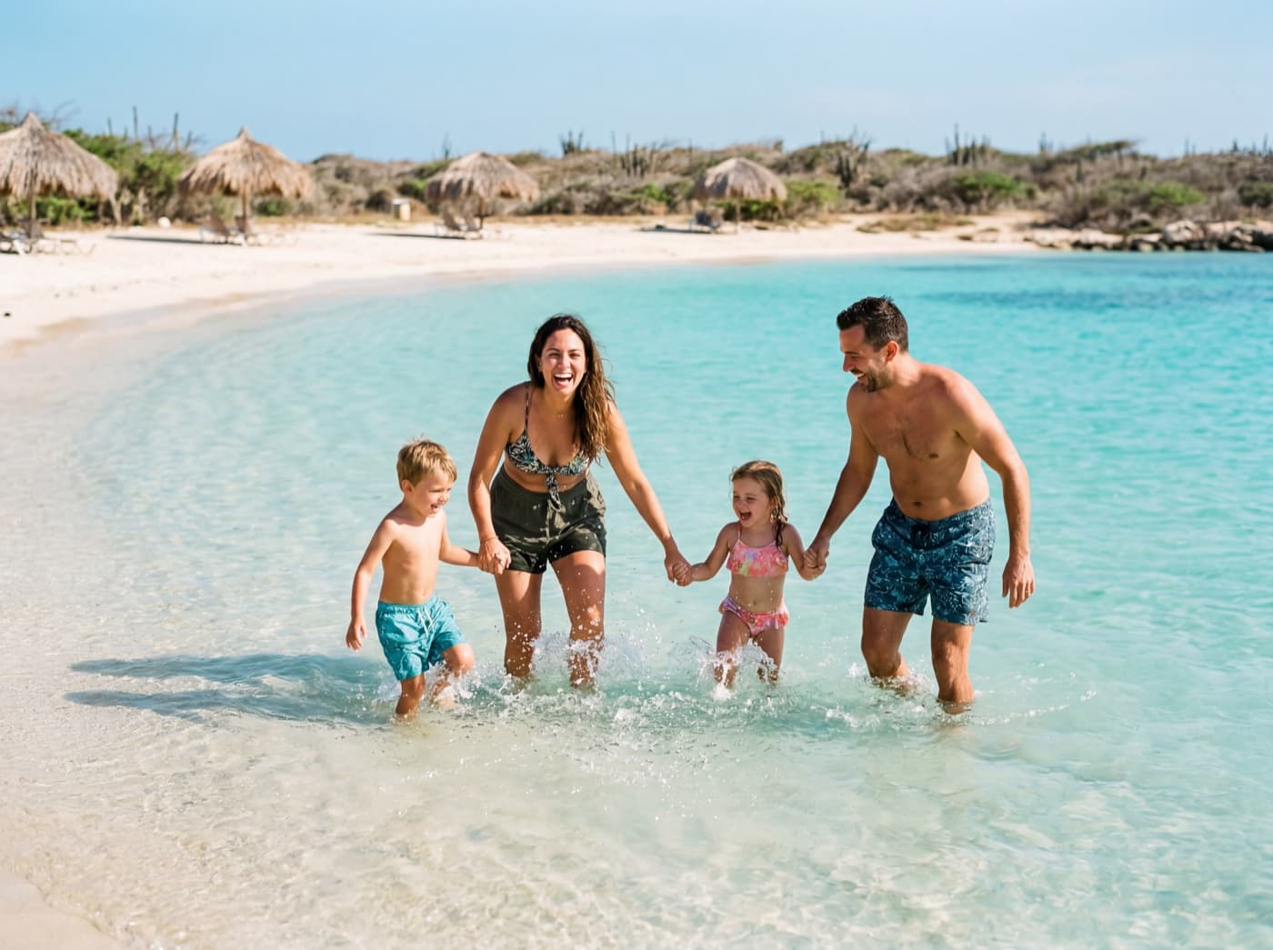 A family laughing together in the clear turquoise shallows of an Aruba beach