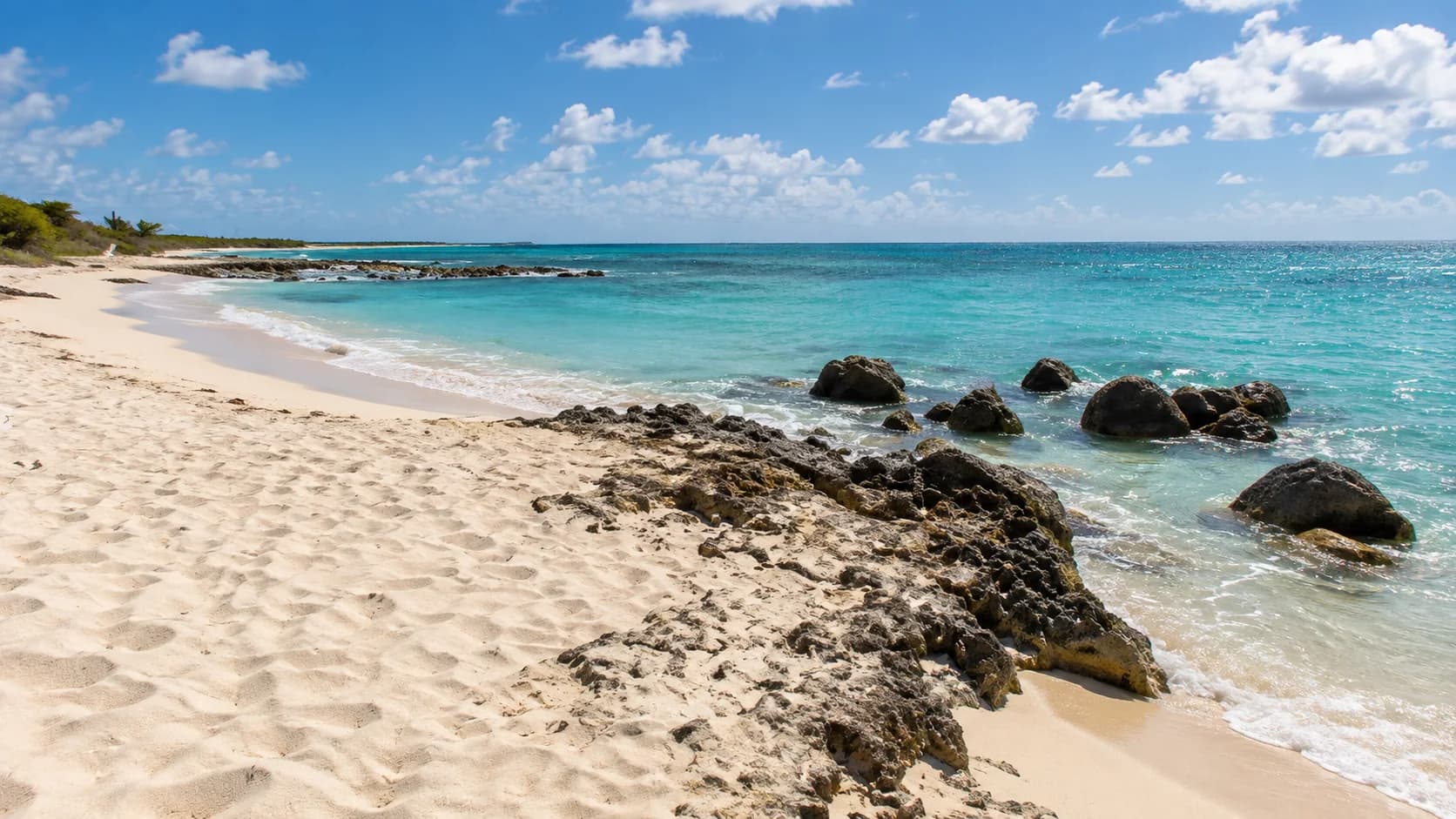 Sand, shallow turquoise water and low limestone rocks along the central shore of Arashi Beach, Aruba