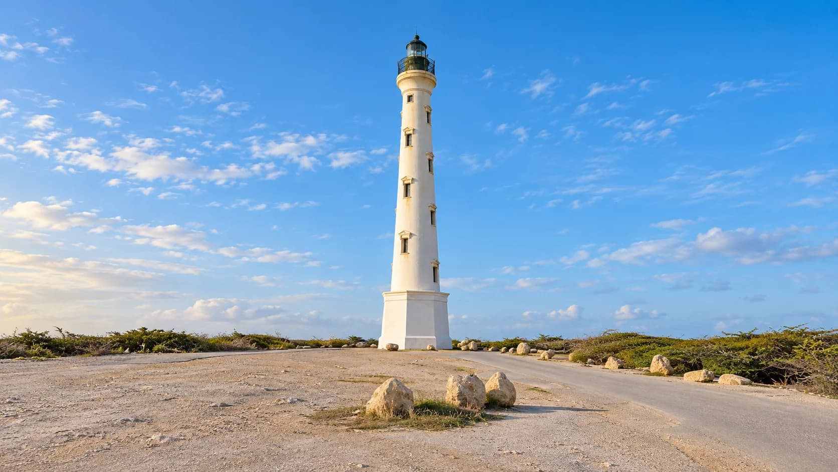 California Lighthouse from the western parking area, with the full white tower, roadside boulders and dry low scrub